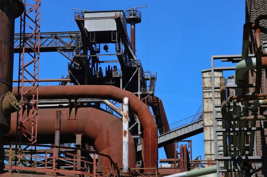 The Art of Drawing Readers In: Your attractive post title goes here Detailed view of an industrial complex featuring rusted steel pipes and structures under a clear blue sky.